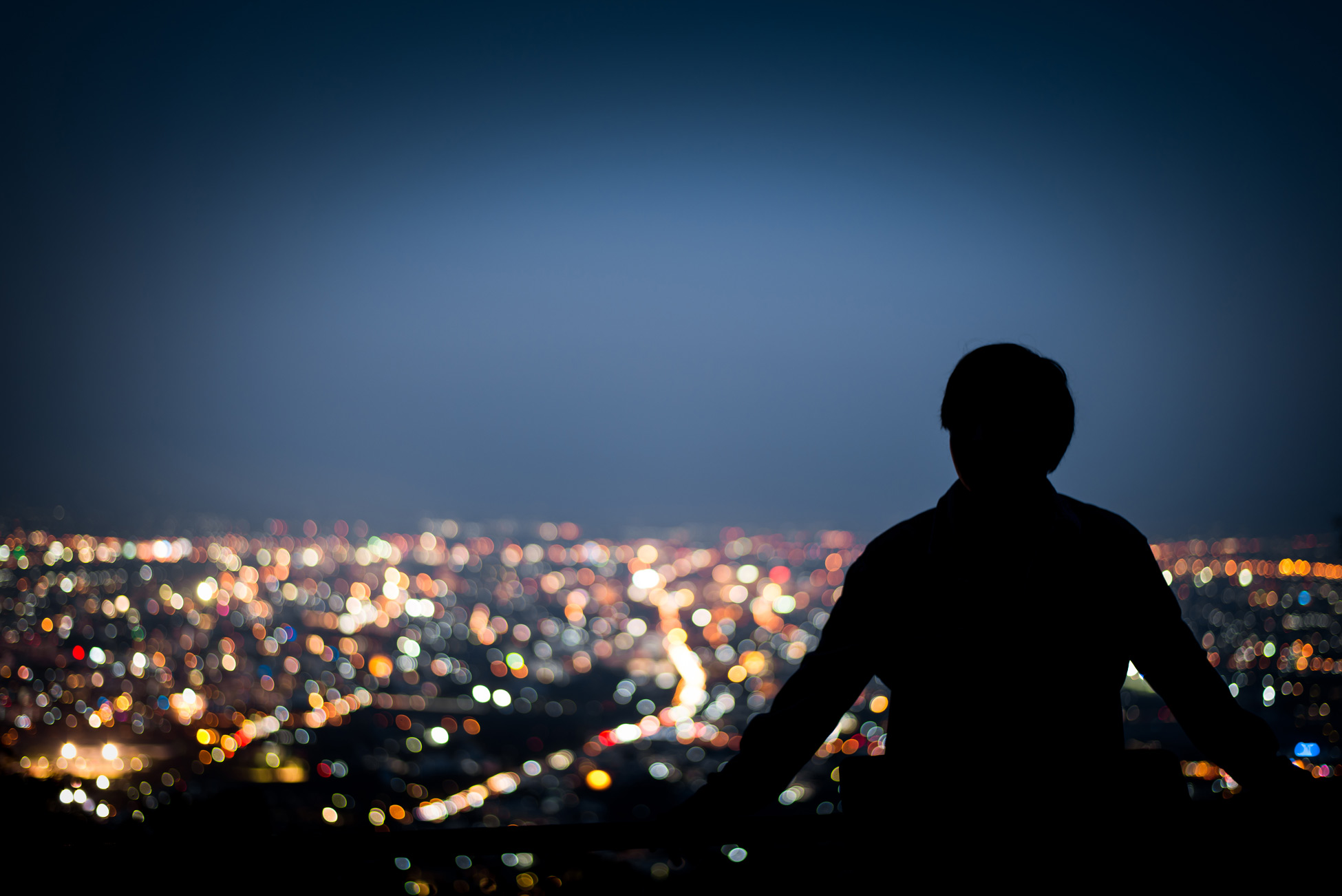 Silhouette von einem Mann, der bei Nacht auf eine Großstadt blickt